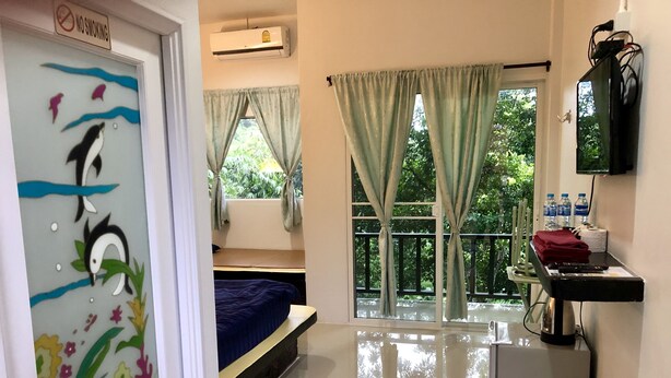 Habitación de hotel con cama, un pequeño escritorio con teclado, un espejo y una ventana con cortinas.