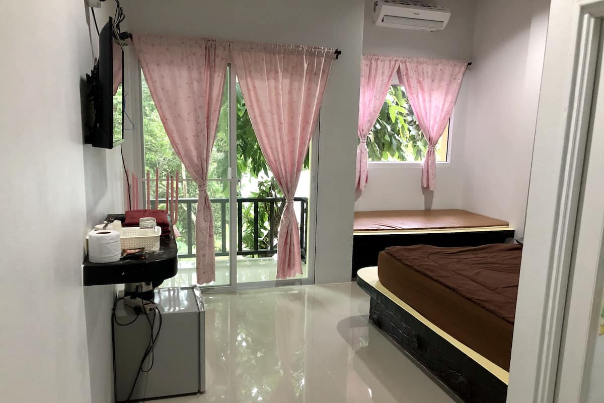 Un dormitorio con una cama, un escritorio pequeño con una computadora y una ventana con cortinas.