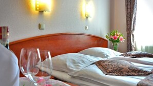 A hotel room with a wooden headboard, a bed with white linens, a vase with flowers, and wall-mounted lights. - Borrowdale Country Manor (Harare)