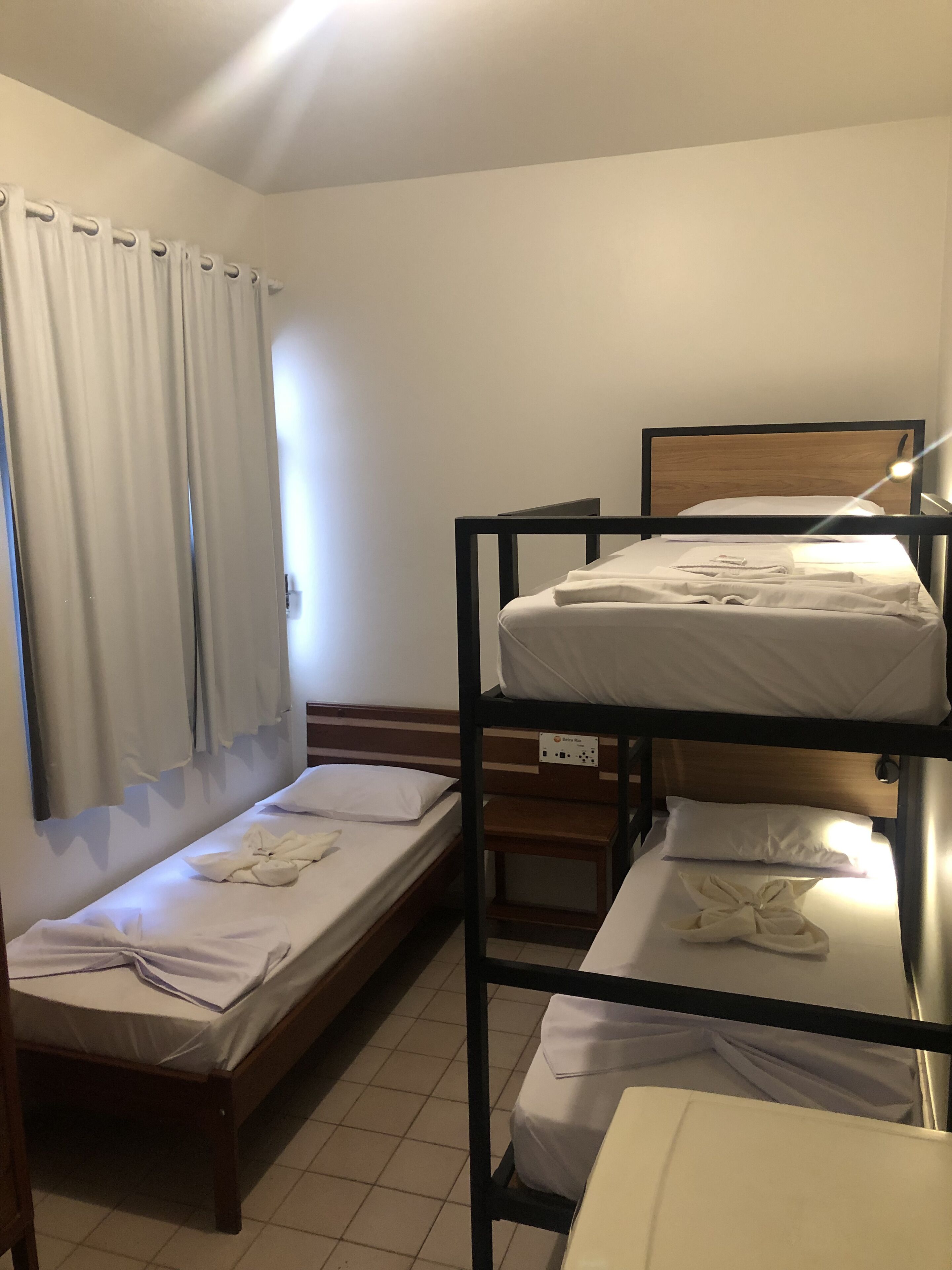 Un dormitorio con literas, una ventana con cortinas y una mesita de noche con lámpara.