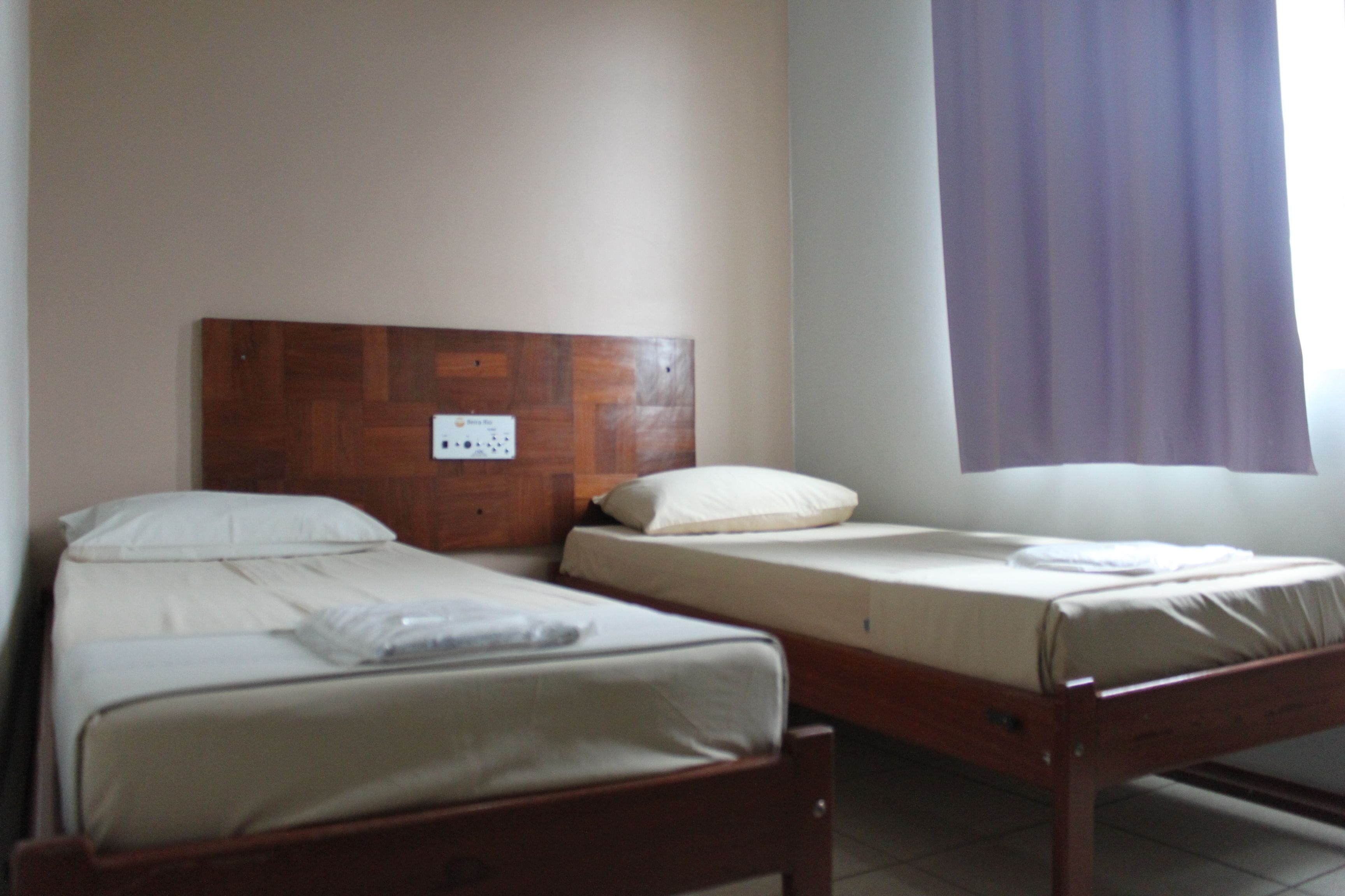 A room with two single beds, wooden headboards, and a window with purple curtains.