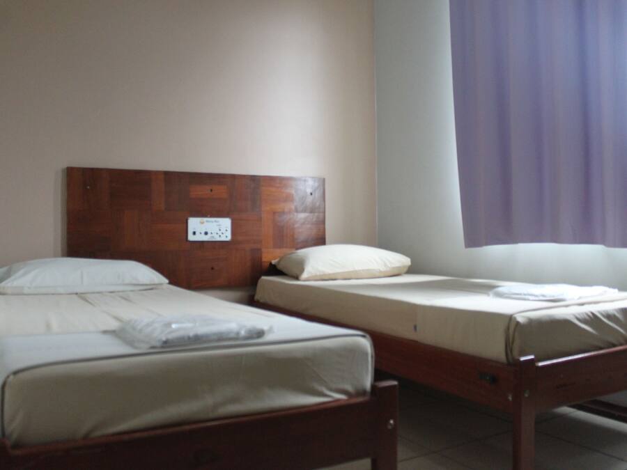 A room with two single beds, wooden headboards, and a window with purple curtains.