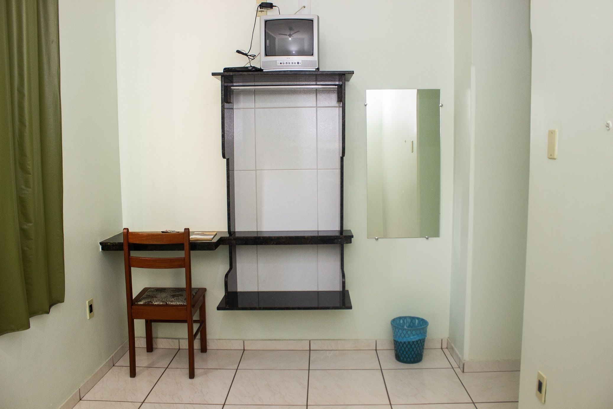 A small room with a desk, chair, and a television on a shelf.