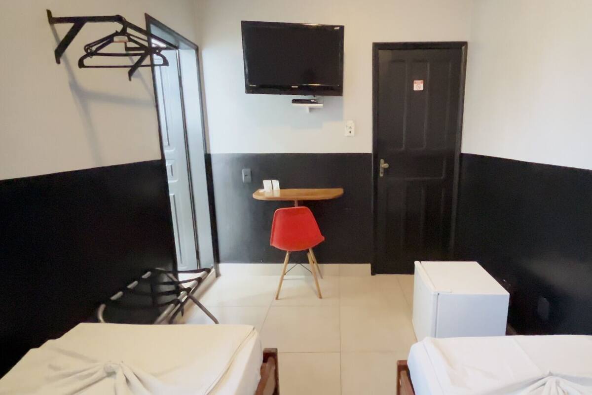 Ein Hotelzimmer mit zwei Betten, einem an der Wand montierten Fernseher, einem roten Sessel und einem kleinen Tisch.