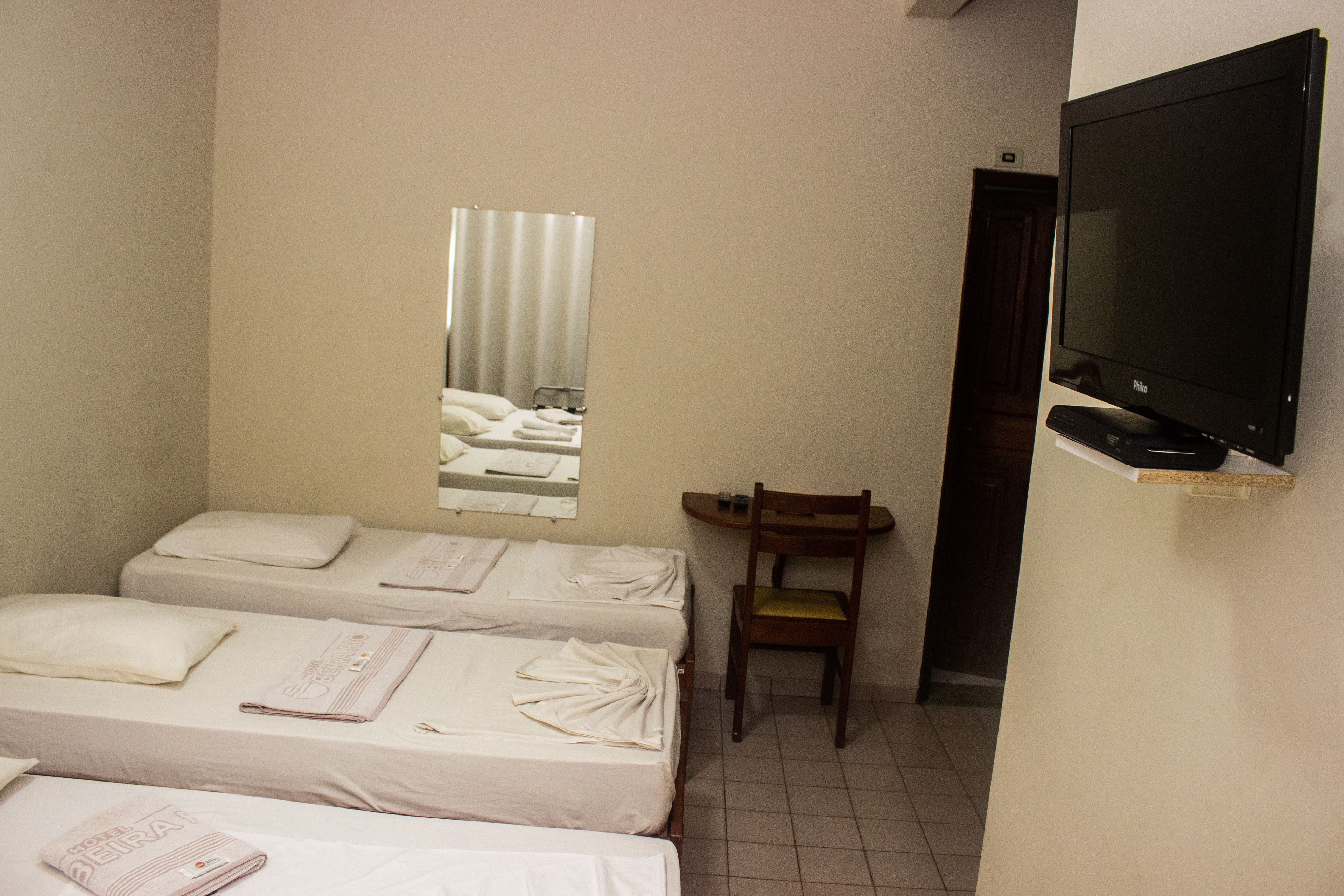 A hotel room with two beds, a television, a mirror, and a chair.