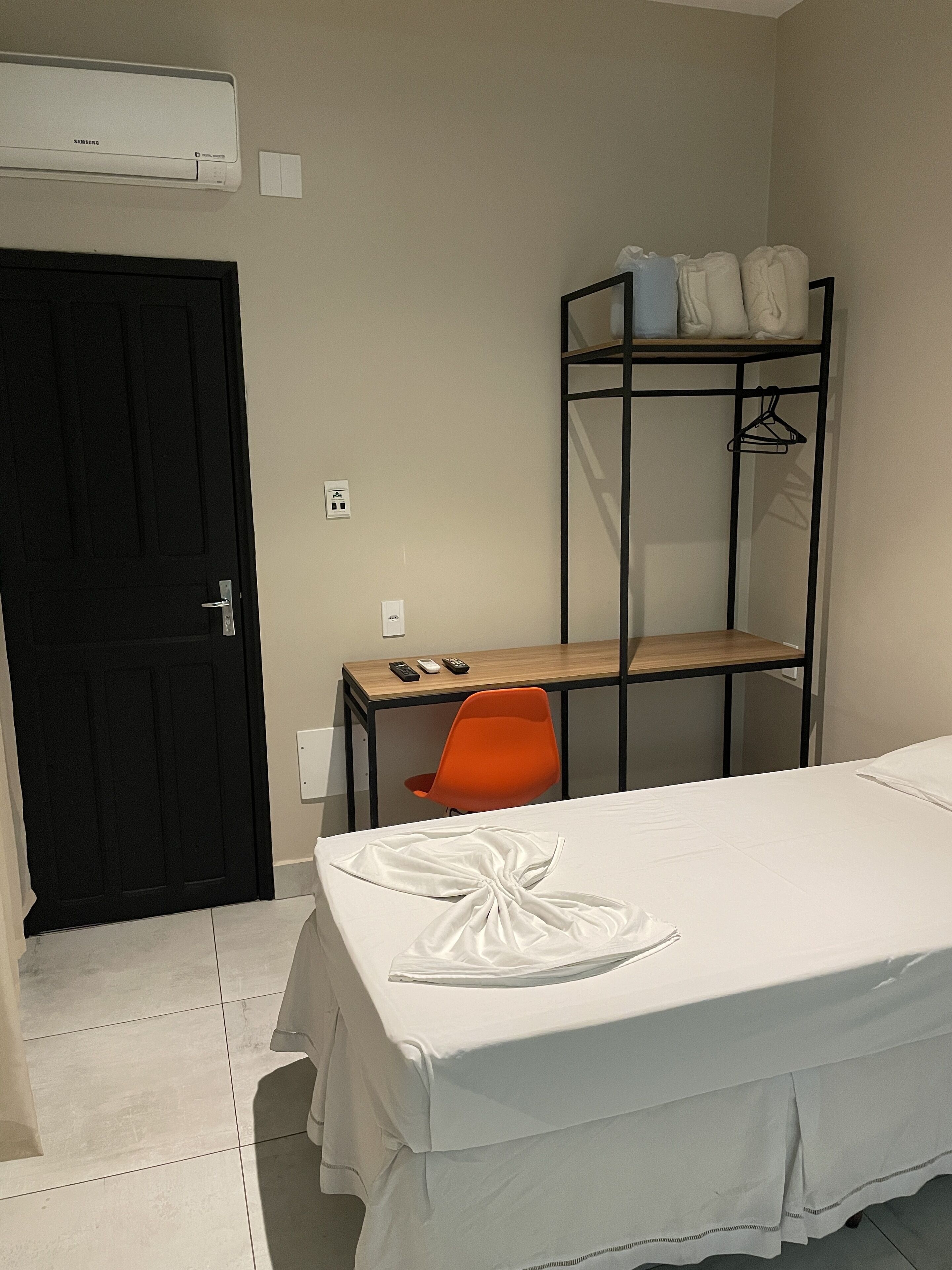 Une chambre à coucher avec un lit, un bureau, une chaise orange, une porte noire et un appareil de climatisation blanc.