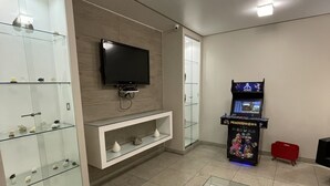 Une chambre moderne équipée d’un téléviseur à écran plat fixé au mur, d’une vitrine en verre contenant des objets décoratifs, d’une petite table avec un plateau en verre et d’une console de jeux Atari.