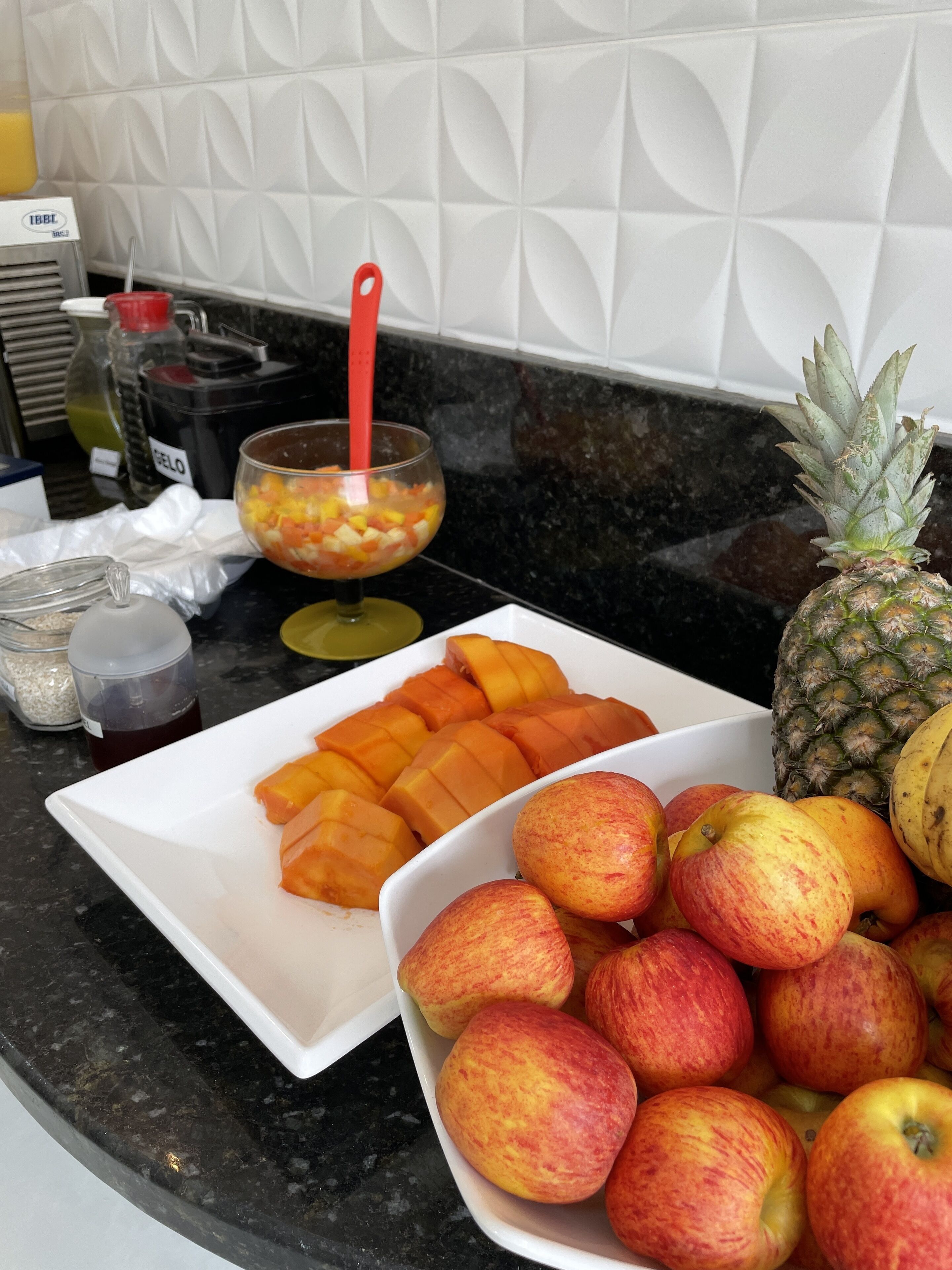 A kitchen counter with a white cutting board, a bowl of diced fruit, and a pineapple.