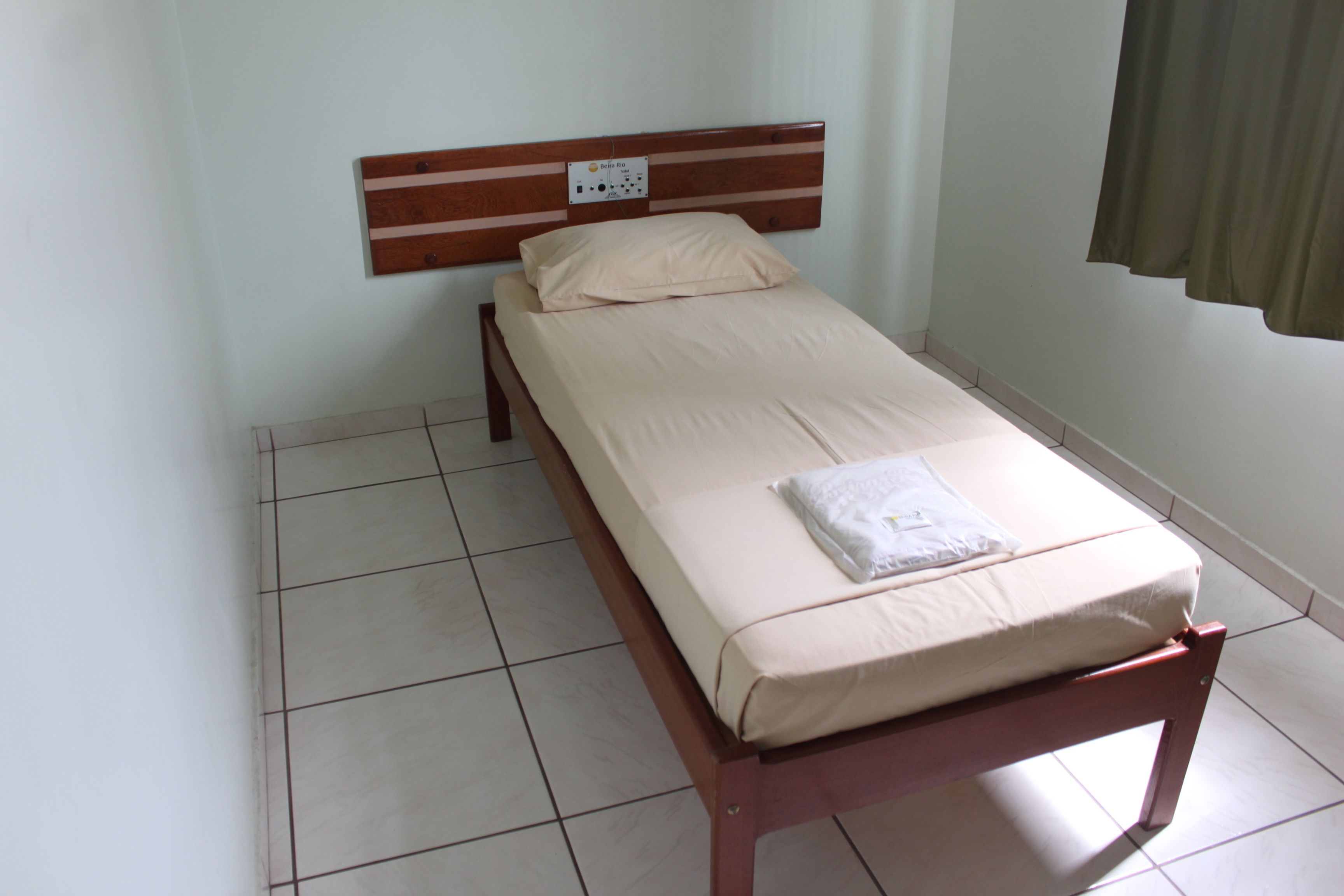 A single bed with a wooden headboard, a beige mattress, and a white pillow.