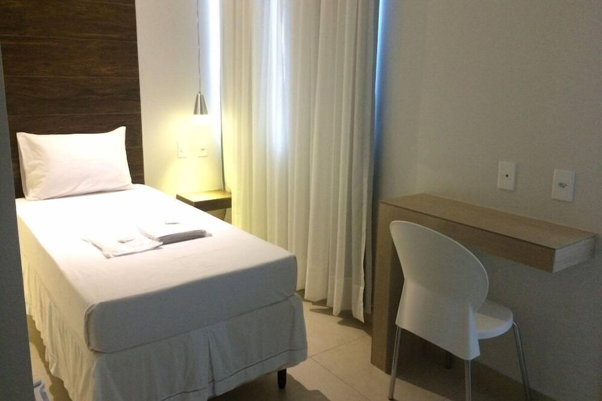 Ein Hotelzimmer mit Bett, Schreibtisch, Stuhl, Nachttisch und einem Fenster mit Vorhängen.
