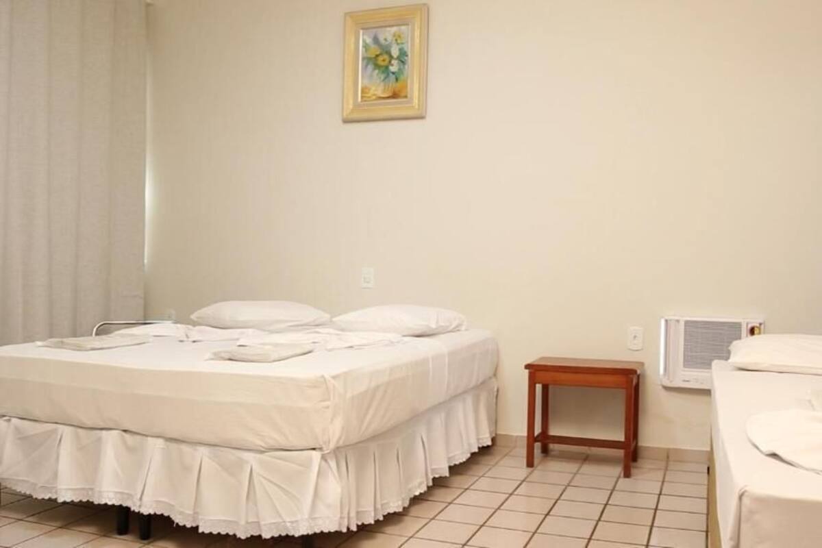 Ein Hotelzimmer mit zwei Betten, einem kleinen Holztisch, einem Bild an der Wand und einem Fenster mit Vorhängen.