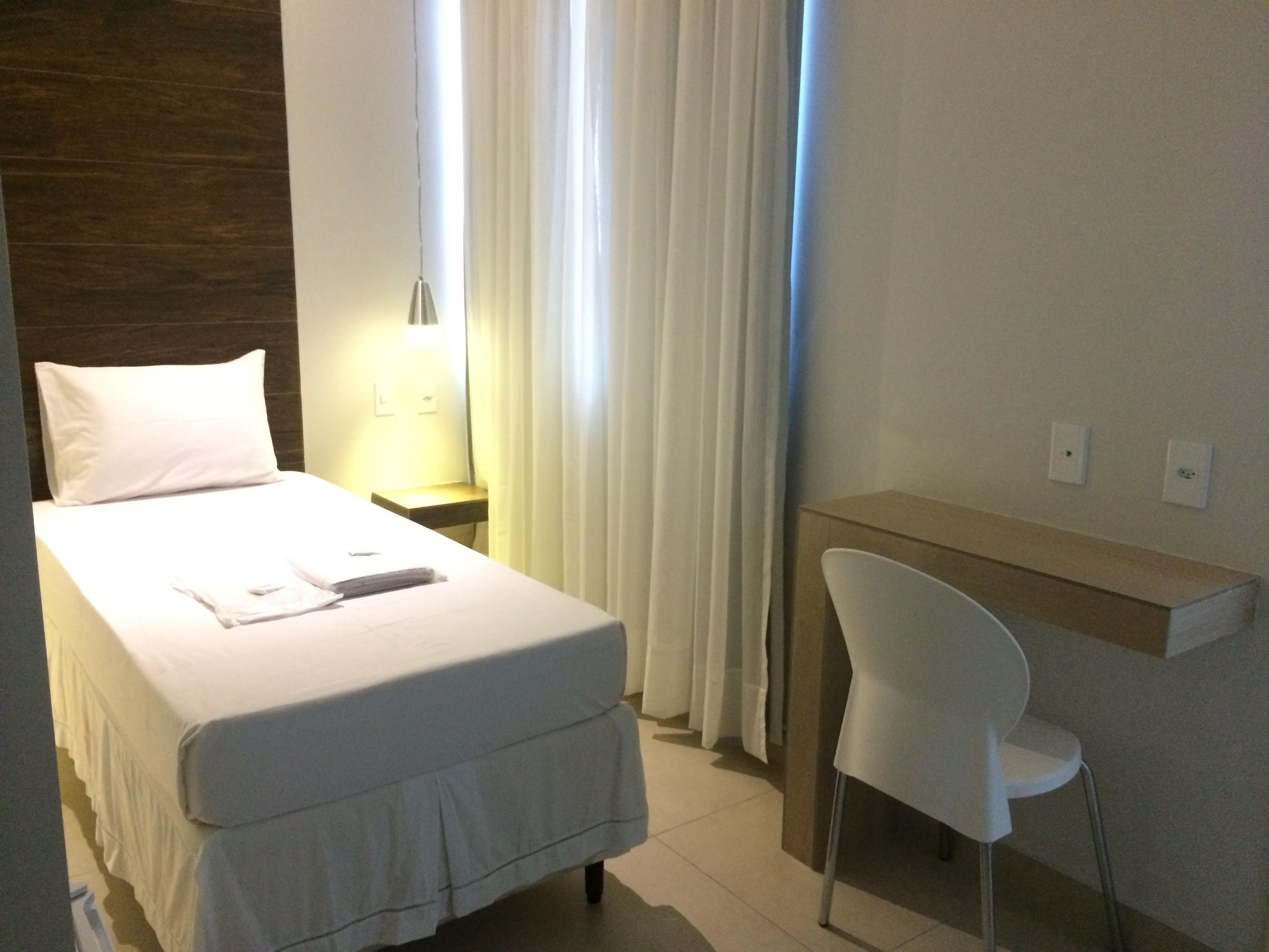 Ein Hotelzimmer mit Bett, Schreibtisch, Stuhl und einem Fenster mit Vorhängen.