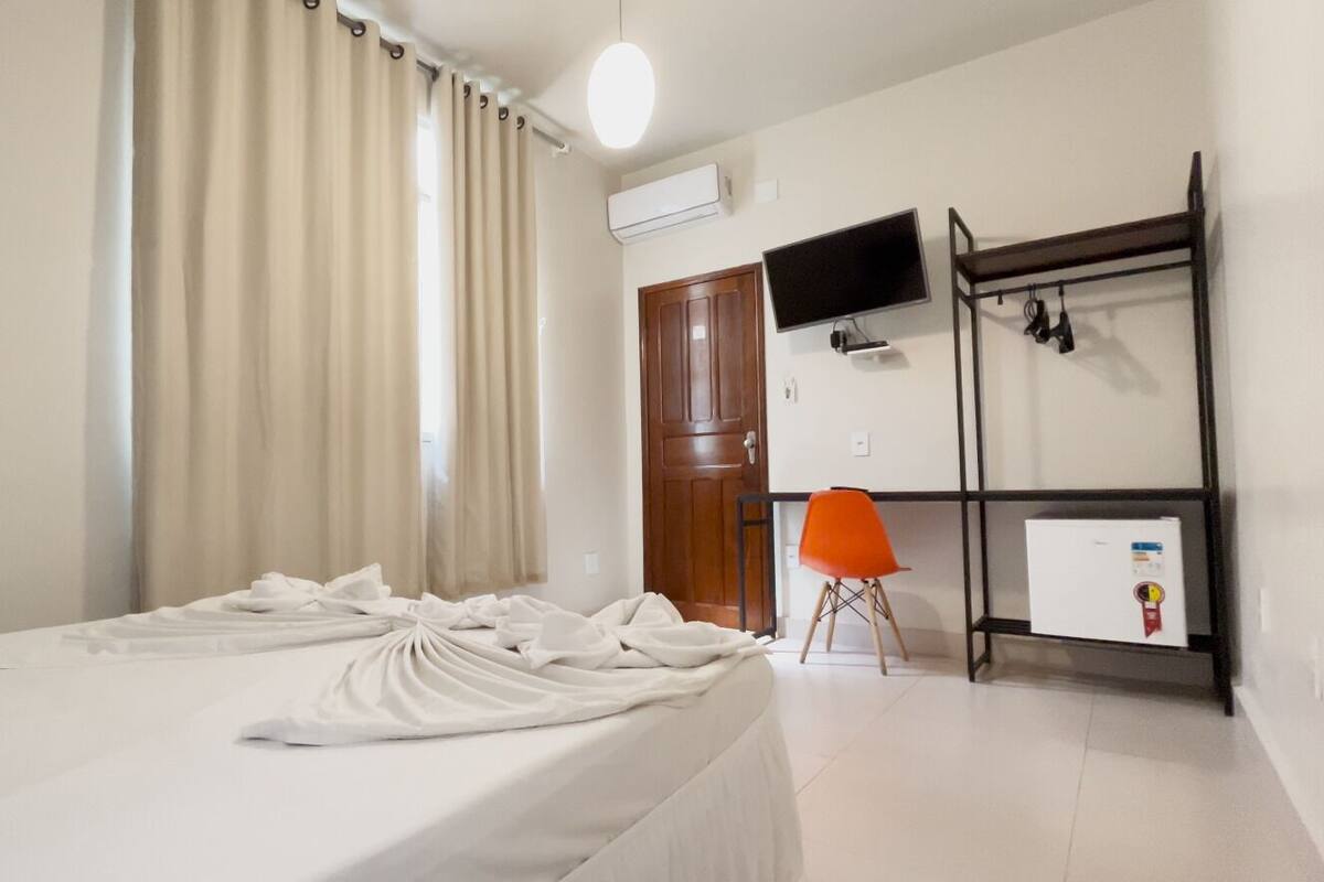 Ein Hotelzimmer mit Bett, Wandfernseher, Kleiderschrank und einem kleinen Tisch mit Stuhl.