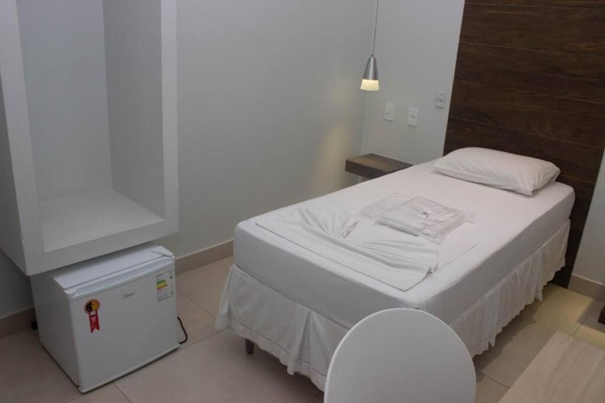 Ein kleines, sauberes Zimmer mit einem Einzelbett, einem Nachttisch, einem kleinen Heizgerät und einer Pendelleuchte.