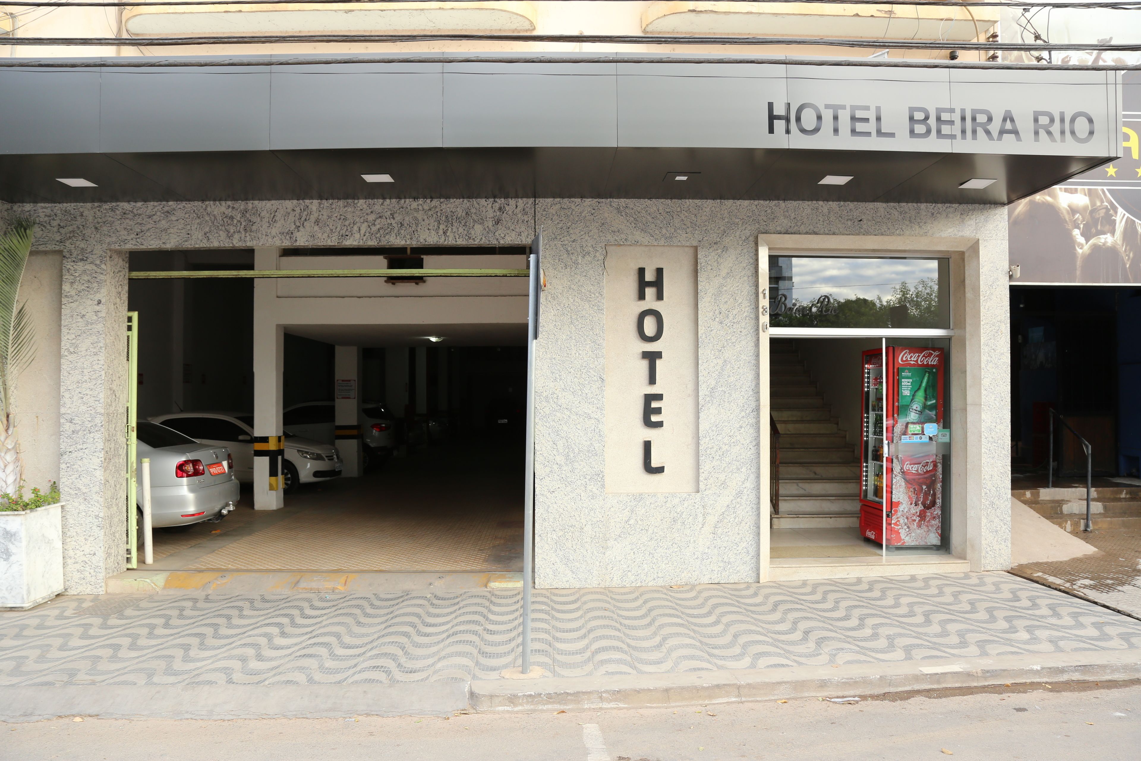 Entrada de un hotel con un cartel que dice "HOTEL BEIRA RIO" y una máquina expendedora de Coca-Cola.