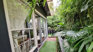 Une terrasse en bois avec un espace recouvert d’un gazon synthétique vert, entouré d’une végétation luxuriante et de grandes plantes.