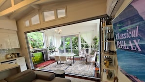 Un vaste espace de vie comprenant un canapé, une table à manger avec des chaises et une vue sur un jardin luxuriant, grâce à de grandes fenêtres.