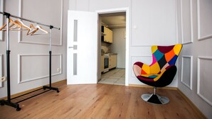 Una habitación con piso de madera, una silla con un diseño geométrico de colores y un perchero con colgadores.