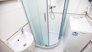 Un baño con ducha envuelta en vidrio, un lavamanos y una lavadora.