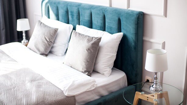 A neatly made bed with a teal headboard, white bedding, and two bedside lamps. - SF Central Apartments (Lviv)