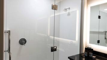 Ein modernes Badezimmer mit einer Duschkabine aus Glas, einer schwarzen Ablagefläche und einem großen Spiegel.