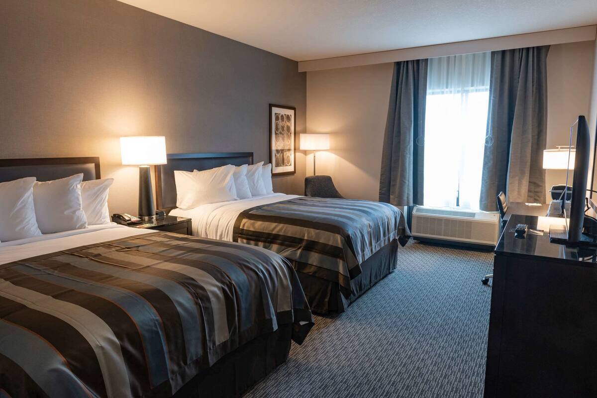 A hotel room with two beds, a desk, a chair, a TV, and a window with curtains.