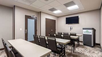 A conference room with multiple tables and chairs, a television mounted on the wall, and a podium with the logo "Wingate by Wyndham".