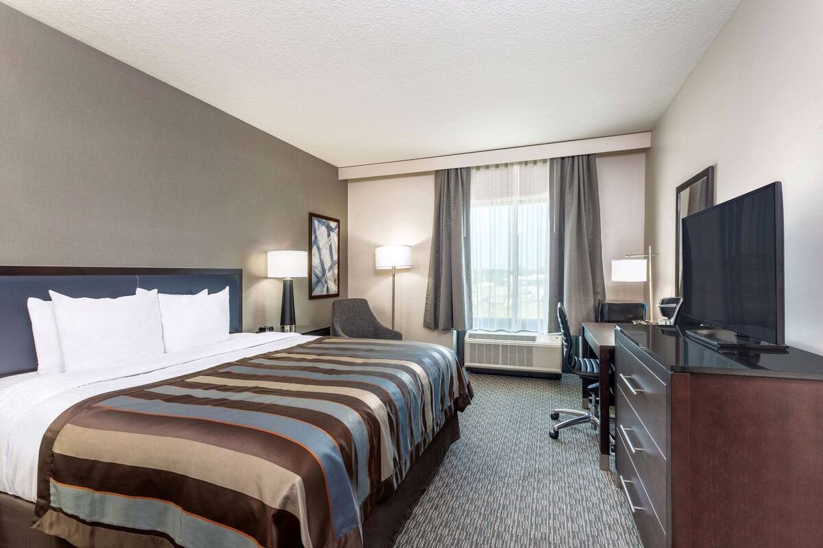 A hotel room with a bed, desk, chair, television, and air conditioning unit.