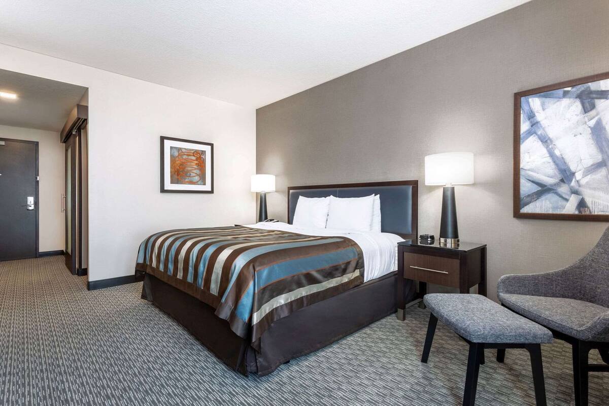 A hotel room with a bed, bedside tables, a chair, and artwork on the walls.