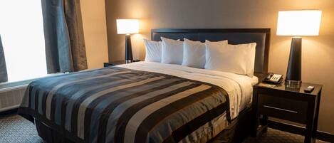 A hotel room with a large bed, two bedside lamps, a nightstand with a phone, and a window with curtains.