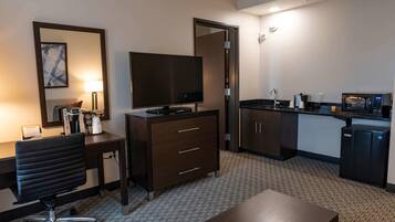 Habitación de hotel con escritorio, silla, televisor, minibar y kitchenette.
