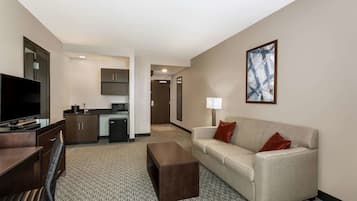 A hotel room with a sofa, a coffee table, a TV, a desk, and a kitchenette.
