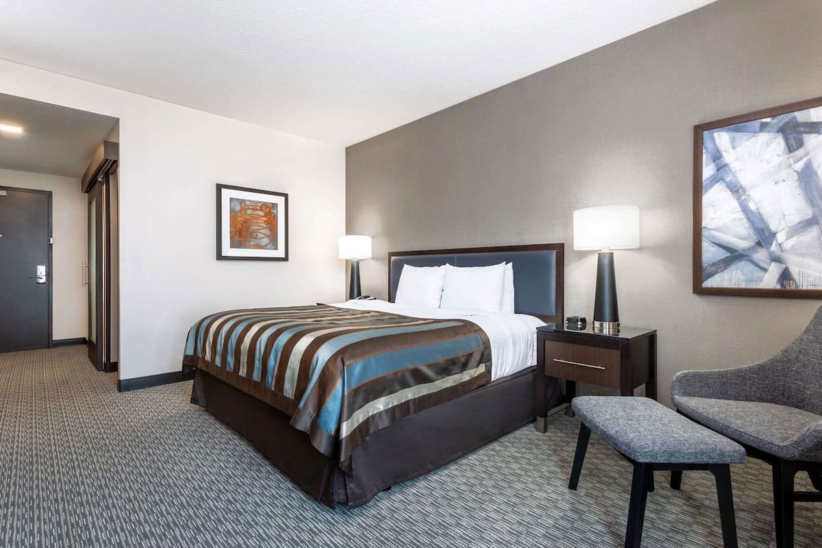 A hotel room with a bed, bedside tables, a chair, and artwork on the walls.