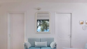 Una habitación con un sofá azul claro a rayas, una mesa redonda blanca y una ventana con vistas a árboles.