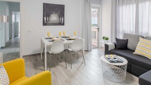 Ein modernes Wohnzimmer mit Essbereich, einer Couch, einem kleinen runden Tisch und Blick durch eine Tür.