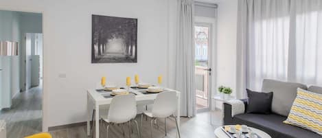 A modern living room with a dining area, a sofa, a small round table, and a view through a door.