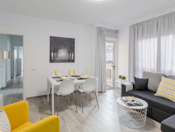 Una sala de estar moderna con comedor, un sofá, una mesita redonda y vista a través de una puerta.