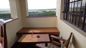 Ein Eckzimmer mit einer hölzernen Sitzbank, einem kleinen Tisch mit einer Vase und einem Buch sowie einem Fenster mit Blick auf eine Landschaft.
