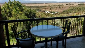 Ein Balkon mit rundem Tisch und zwei Stühlen, mit Blick auf eine Landschaft mit Bäumen und weit entfernten Gebäuden.