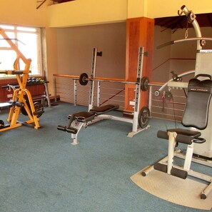 Uma academia com diversos equipamentos de exercícios, incluindo um banco prensa, uma estrutura para agachamento e um aparelho de polia.