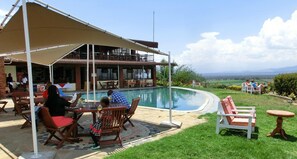 Área de piscina ao ar livre com espaço de estar coberto, piscina e vista para a paisagem.