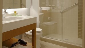 Ein modernes Badezimmer mit einer Duschkabine aus Glas, einem weißen Waschbecken mit Spiegel darüber und einer Holz-Kommode.
