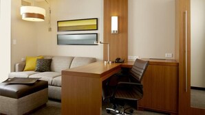 Ein Hotelzimmer mit einem Holztisch, einem Ledersessel, einer Couch mit Kissen, einem Laptop auf einem Beistelltisch und zwei Wandleuchten.