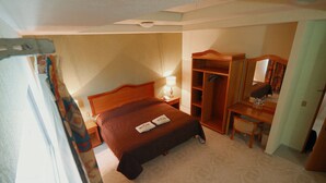 A hotel room with a bed, a desk, a wardrobe, and a mirror. - Hotel El Conquistador Monarca (Zitácuaro)
