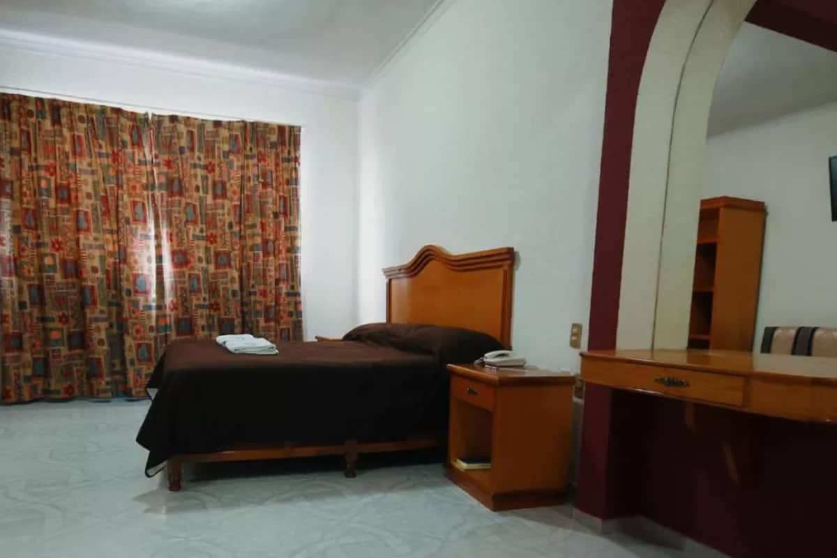 A bedroom with a bed, a nightstand, a dresser, a mirror, and a window with curtains.