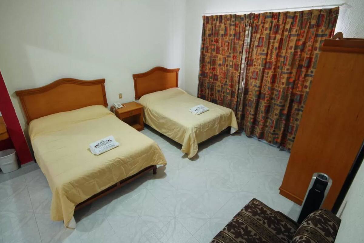 A room with two beds, a wooden headboard, a patterned curtain, and a small table.