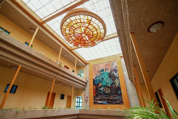 A multi-level atrium with a large stained glass ceiling, a mural, and a fire extinguisher. - Hotel El Conquistador Monarca (Zitácuaro)