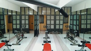 A gym with exercise equipment, mirrors, and a red bench. - Hotel El Conquistador Monarca (Zitácuaro)
