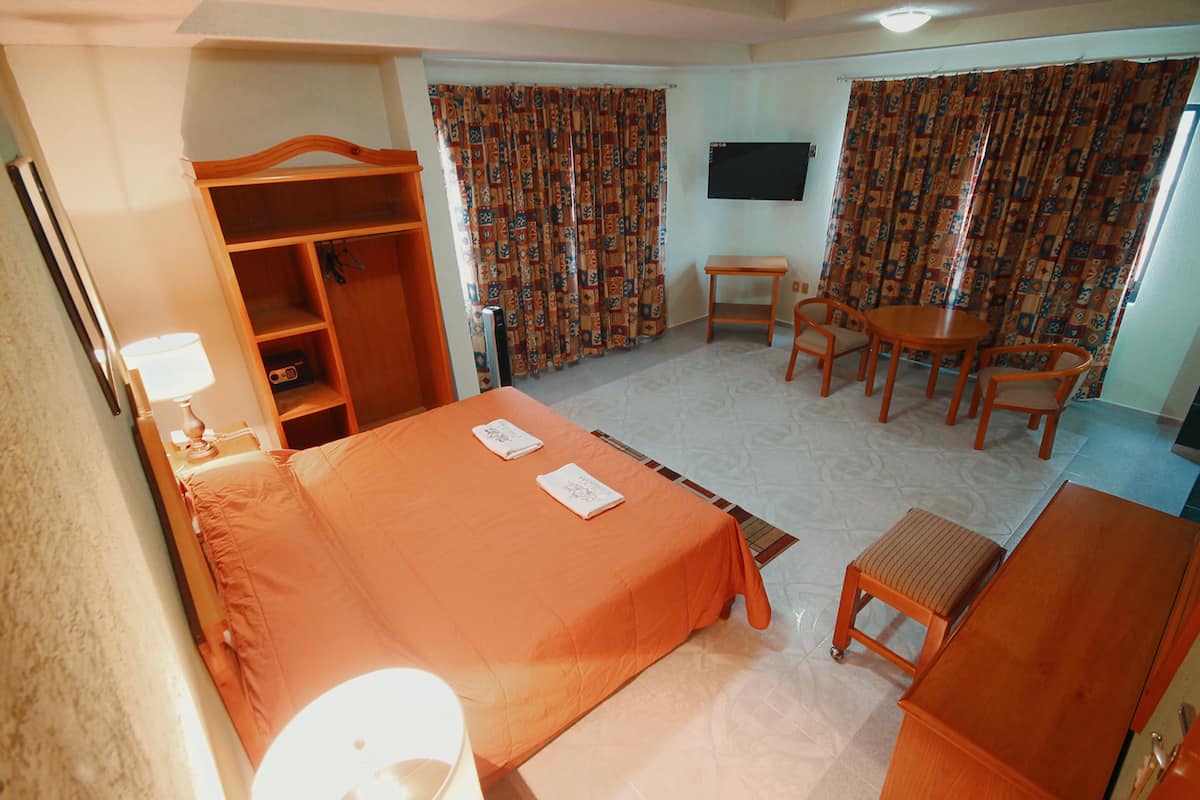 A hotel room with a bed, a desk, a chair, a small table, a wardrobe, and a television.