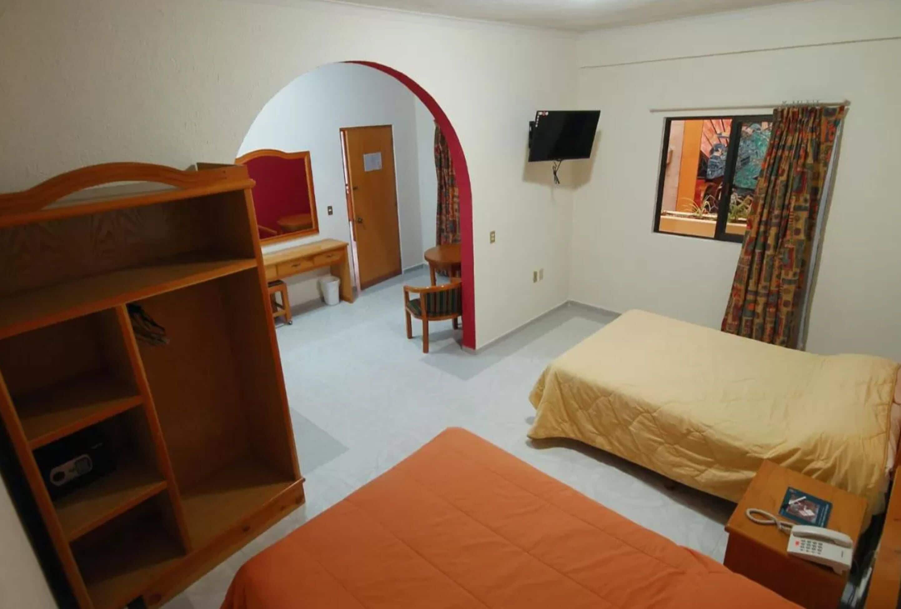 A hotel room with a bed, a desk, a chair, a TV, and a window with curtains.